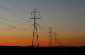 Electricity transmission towers silhouetted against a sunset, representing the power grid strain behind New York data center policy