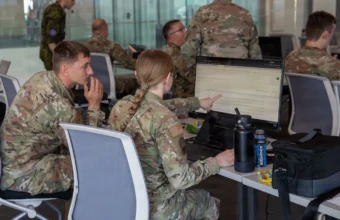 Two soldiers analyze defensive data logs together on a computer terminal, one pointing at a line on screen, representing how the right context changes what an AI agent can diagnose