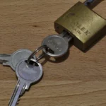 A brass padlock with two matching keys resting on a wooden surface