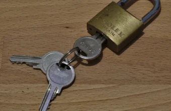 A brass padlock with two matching keys resting on a wooden surface