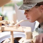 A U.S. Army soldier closely reads a thick technical manual while working on equipment during an equipment issue at Camp Arifjan, Kuwait
