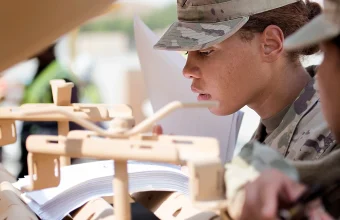 A U.S. Army soldier closely reads a thick technical manual while working on equipment during an equipment issue at Camp Arifjan, Kuwait