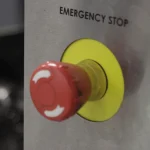 A red mushroom-head emergency stop button labeled Emergency Stop on the stainless steel control panel of a CNC machine