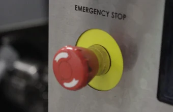 A red mushroom-head emergency stop button labeled Emergency Stop on the stainless steel control panel of a CNC machine