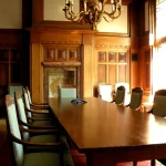 An empty wood-paneled corporate boardroom with a long conference table and rows of chairs