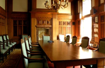 An empty wood-paneled corporate boardroom with a long conference table and rows of chairs