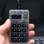 A hand holds a Coinkite Coldcard hardware wallet showing a Bitcoin transaction confirmation screen and numeric keypad