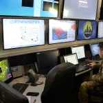 A U.S. Army cyber protection specialist monitors a wall of computer screens showing network defense dashboards during a training exercise