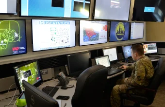 A U.S. Army cyber protection specialist monitors a wall of computer screens showing network defense dashboards during a training exercise