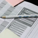 A pencil labeled with standardized test names rests across a multiple-choice answer sheet, evoking the exam analogy behind double-blind AI evaluation