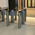 A modern glass optical turnstile with a QR code reader controlling access to an office lobby
