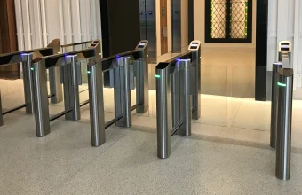 A modern glass optical turnstile with a QR code reader controlling access to an office lobby