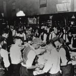 Black and white 1890s photo of postal clerks sorting mail by hand at a crowded sorting table, pigeonhole shelving visible in the background