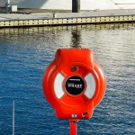 A red emergency life ring safety station mounted on a post beside a marina dock