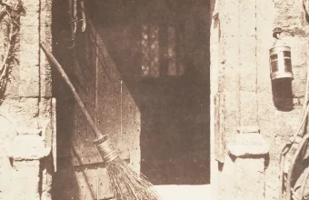 1844 sepia photograph titled The Open Door by William Henry Fox Talbot, showing a rustic open wooden doorway with a broom leaning against it and a lantern on the wall