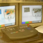 A Smiths Detection X-ray baggage screening console with dual monitors showing false-color scans of the contents of a bag