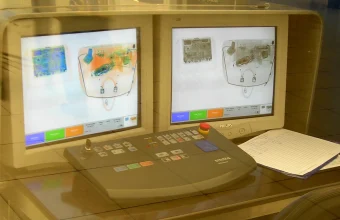 A Smiths Detection X-ray baggage screening console with dual monitors showing false-color scans of the contents of a bag