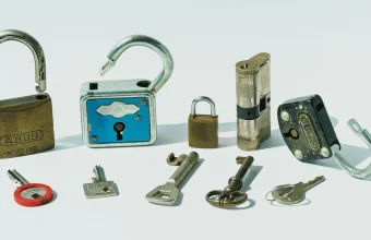 Six antique padlocks of different shapes and sizes with six mismatched keys laid out on a white background