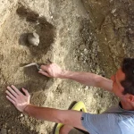 An archaeologist uses a trowel to carefully excavate a small pot from the soil, a visual metaphor for uncovering a legacy codebase's buried context before making changes