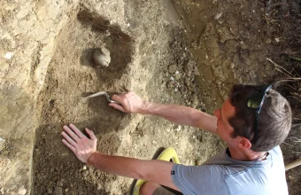 An archaeologist uses a trowel to carefully excavate a small pot from the soil, a visual metaphor for uncovering a legacy codebase's buried context before making changes