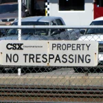 A CSX Transportation No Trespassing sign mounted on a chain-link fence beside railroad tracks