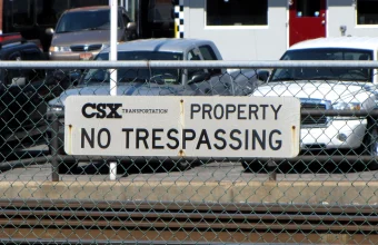 A CSX Transportation No Trespassing sign mounted on a chain-link fence beside railroad tracks