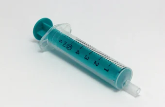 A clear and teal 5ml single-use medical syringe lying diagonally on a white background, used as a visual metaphor for SQL injection attacks