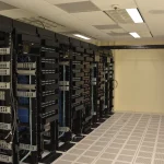 A row of network and server racks with cable management running down a raised-floor data center aisle
