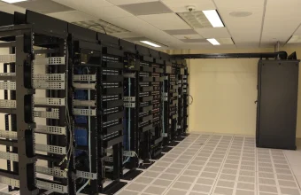 A row of network and server racks with cable management running down a raised-floor data center aisle