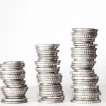 Five stacked piles of coins of increasing height against a white background