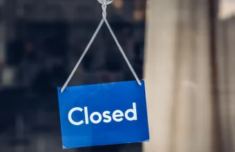 A blue Closed sign hanging inside a glass shop door