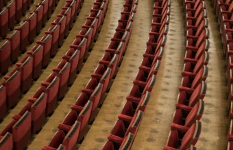 Rows of empty red theatre seats curving toward an empty stage, seen from above