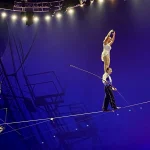 Two Flying Wallendas circus performers balance on a high wire without a net, one standing on the other's shoulders