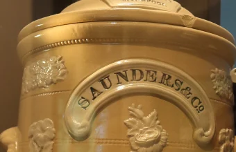 Close-up of an antique ceramic Saunders and Co. gravity water filter urn with ornate floral relief and a branded nameplate, Museum of Liverpool