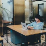 A man works on a laptop at a desk in a modern office coworking space