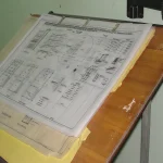 A stack of architectural blueprints on a drafting table, a visual metaphor for designing a GUI form before writing code