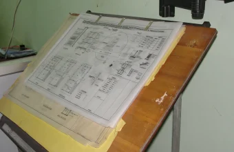 A stack of architectural blueprints on a drafting table, a visual metaphor for designing a GUI form before writing code