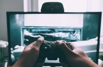 Close-up of hands holding a video game controller in front of a monitor displaying gameplay