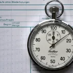 A REFA time-study stopwatch resting on a printed time-recording sheet, representing repeated timed measurements