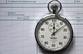 A REFA time-study stopwatch resting on a printed time-recording sheet, representing repeated timed measurements