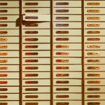 A wall of individually numbered brass safe deposit boxes in a bank vault, each with its own separate keyhole