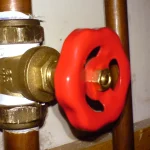 A red gate valve mounted on copper pipes, controlling water flow, used as a visual metaphor for controlling the rate of API requests