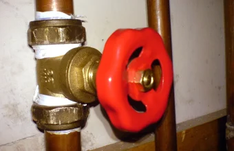 A red gate valve mounted on copper pipes, controlling water flow, used as a visual metaphor for controlling the rate of API requests