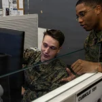 Two U.S. Marines review a monitor together in a Network and Security Operations Center at Marine Corps Base Camp Pendleton