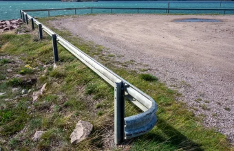 A curved steel highway guardrail running along a rocky coastline