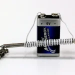 A homemade electromagnet made from a nail wrapped in wire and connected to a 9-volt battery, next to a small pile of nails it can pick up