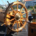 A weathered wooden ship's steering wheel with brass fittings aboard the historic tall ship Star of India in San Diego