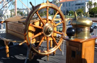 A weathered wooden ship's steering wheel with brass fittings aboard the historic tall ship Star of India in San Diego