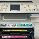 Office multifunction printer with its toner cartridge drawer open, showing yellow and magenta toner cartridges