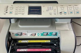 Office multifunction printer with its toner cartridge drawer open, showing yellow and magenta toner cartridges